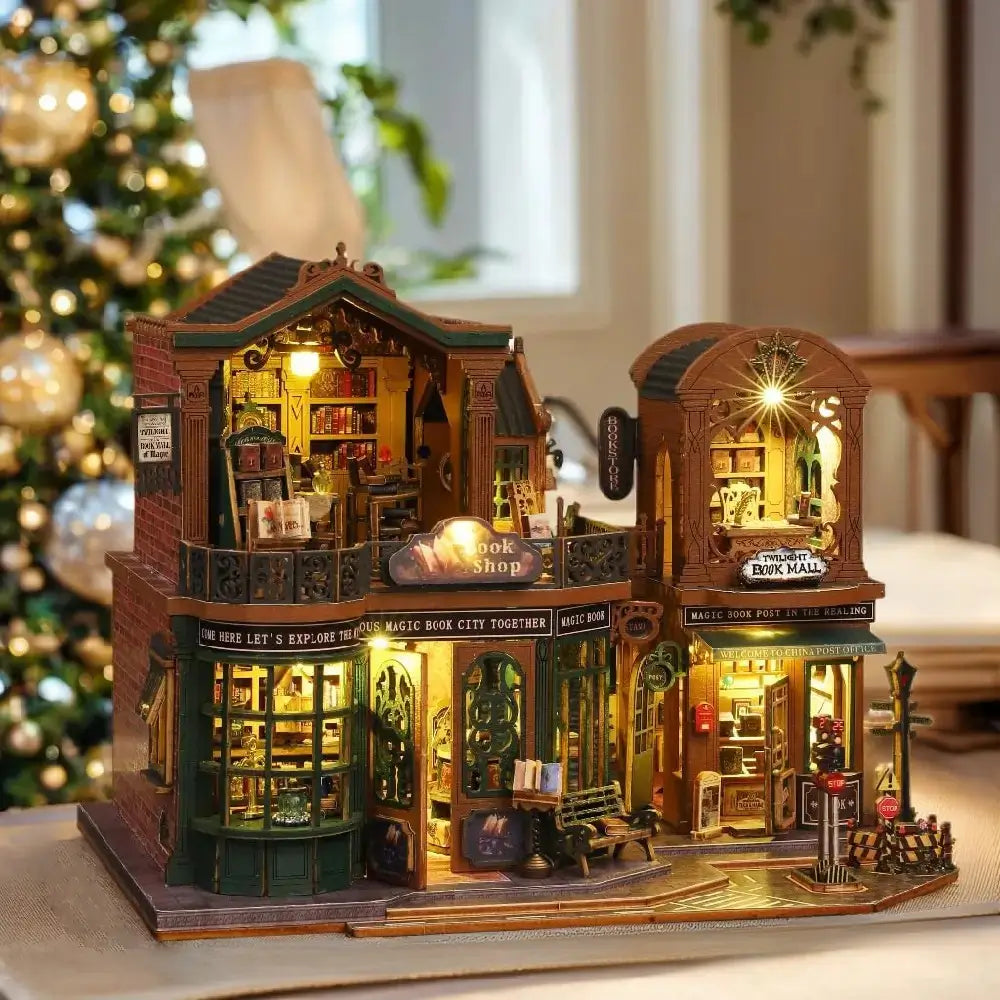 Detailed model of a bookshop with illuminated interior, placed on a surface with a blurred Christmas tree in the background.